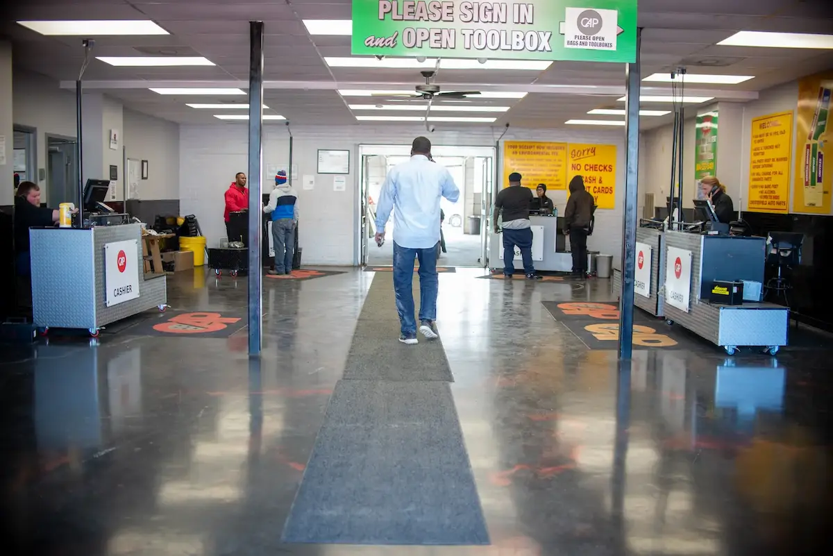 Person talking on phone walking through Chesterfield Auto Parts building under sign reading Please Sign In and Open Toolbox